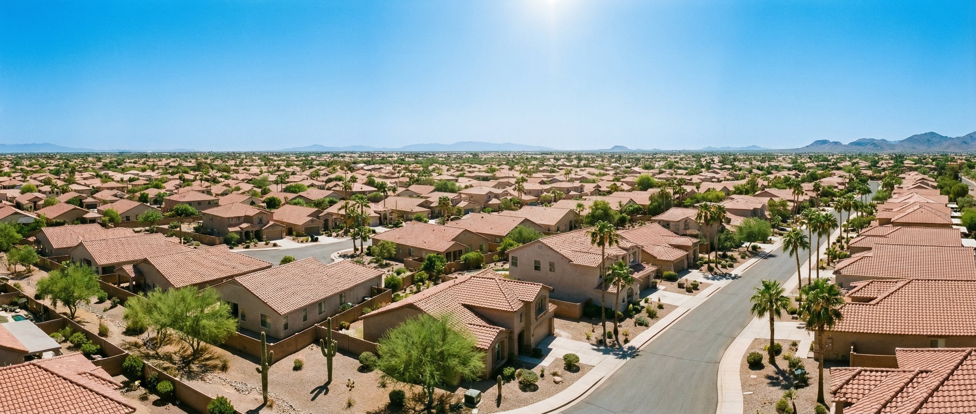 Wide desert landscape view with Phoenix residential neighborhood, stucco homes, terracotta rooftops, and clear blue sky