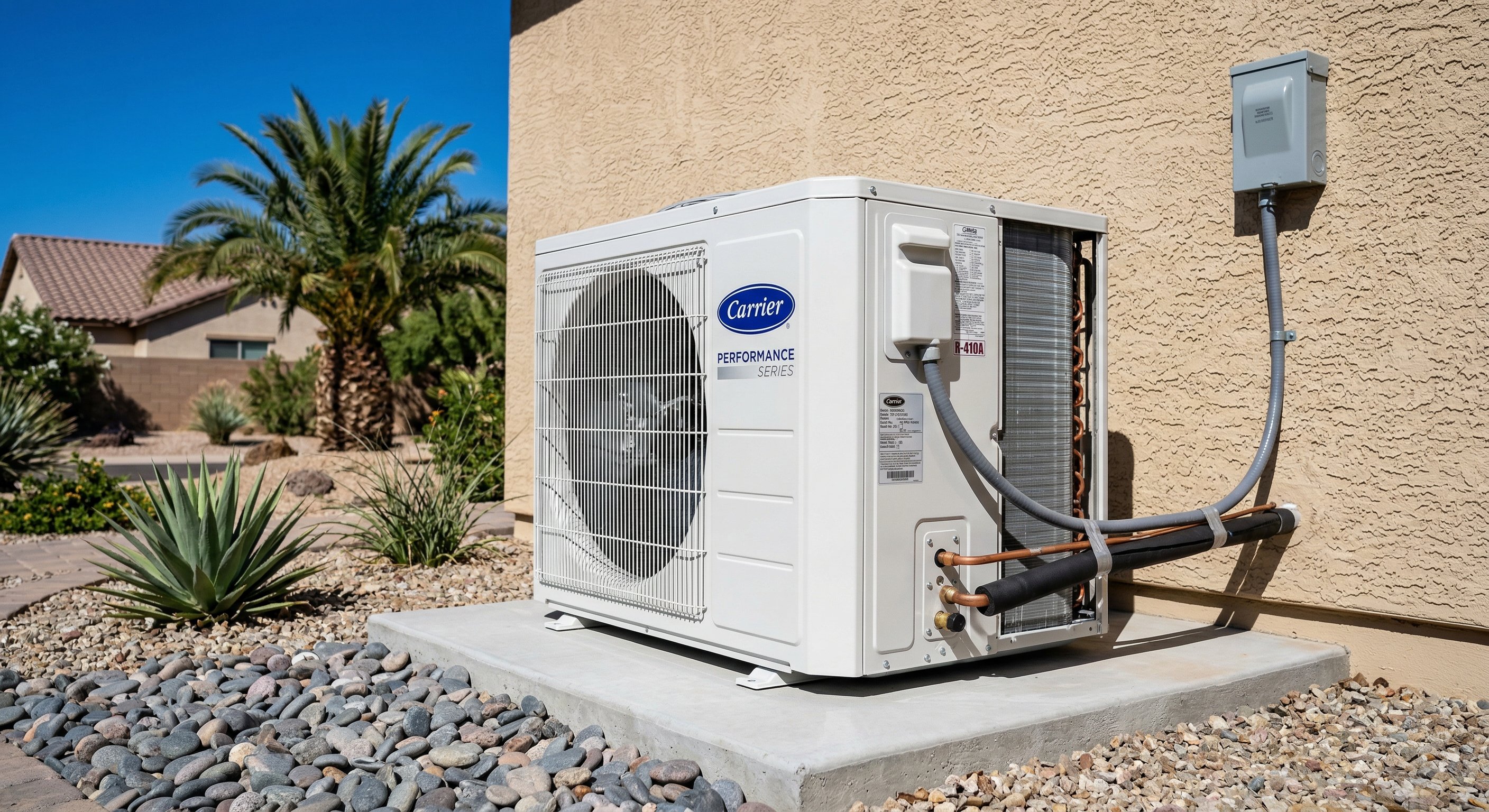 New Carrier AC condenser unit installed on concrete pad next to beige stucco wall in Goodyear AZ, clean desert landscaping, palm tree visible